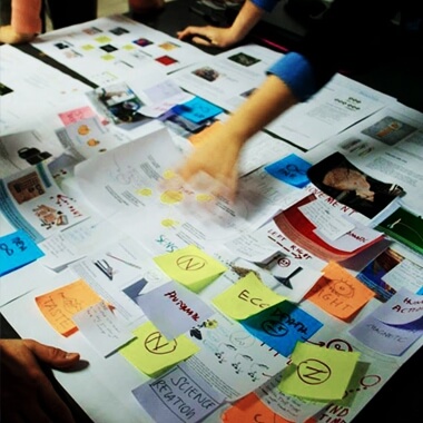 Kreativer Designprozess mit Skizzen, Notizen, Bildern und farbigen Post-its auf einem grossen Arbeitstisch.